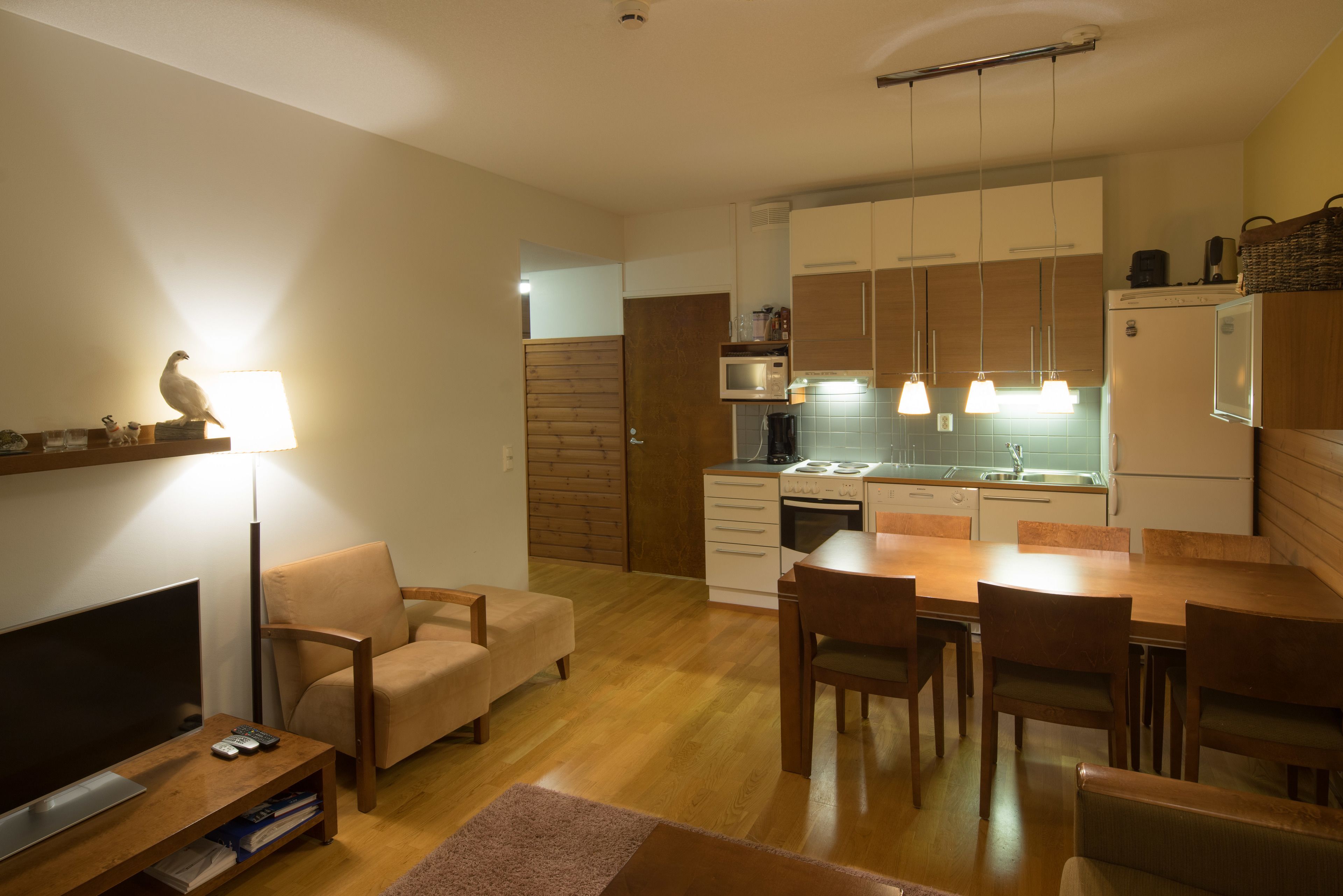 A modern kitchen with wooden cabinets, a dining table, and a TV in the living area.