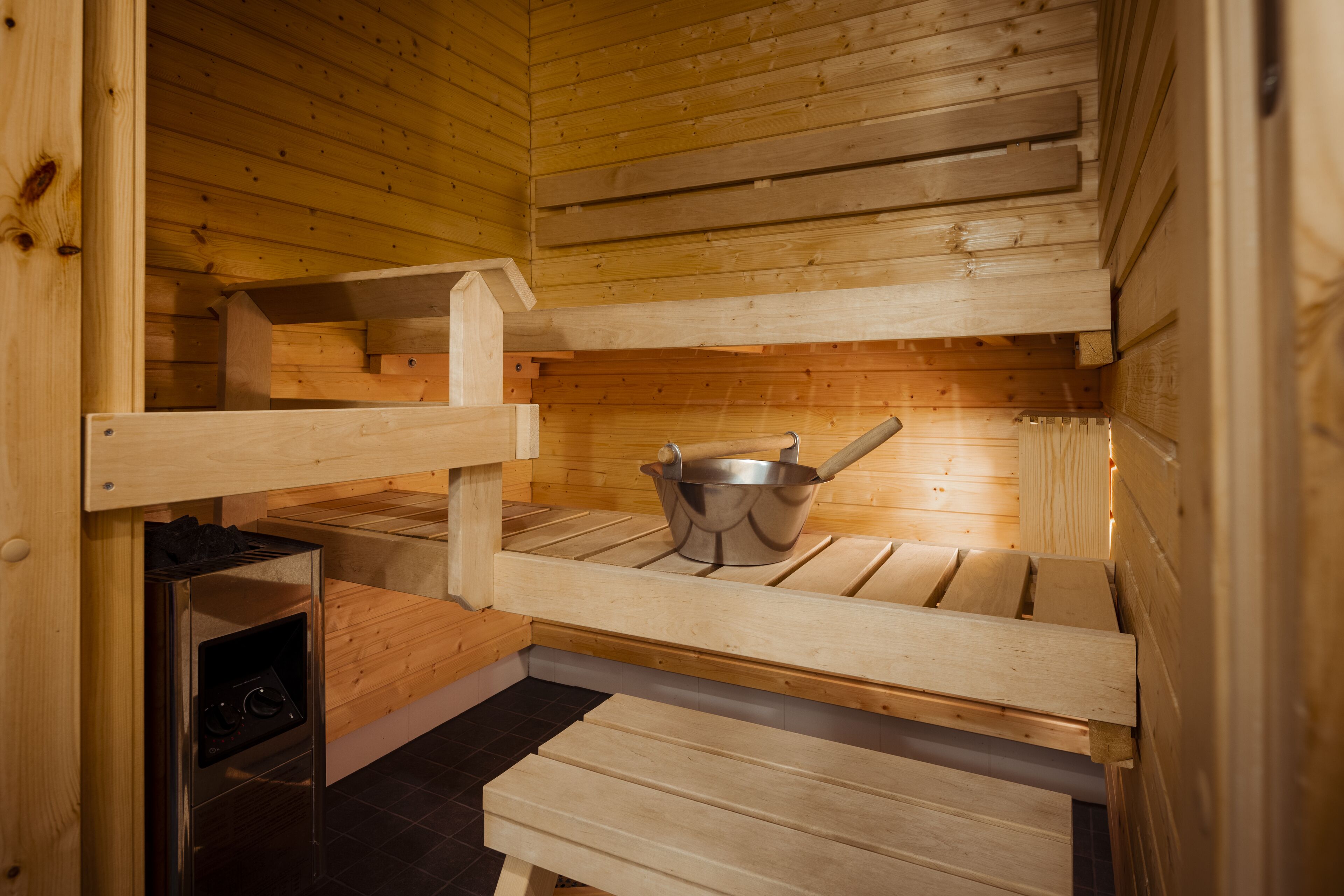 A sauna with wooden benches and a metal bucket.
