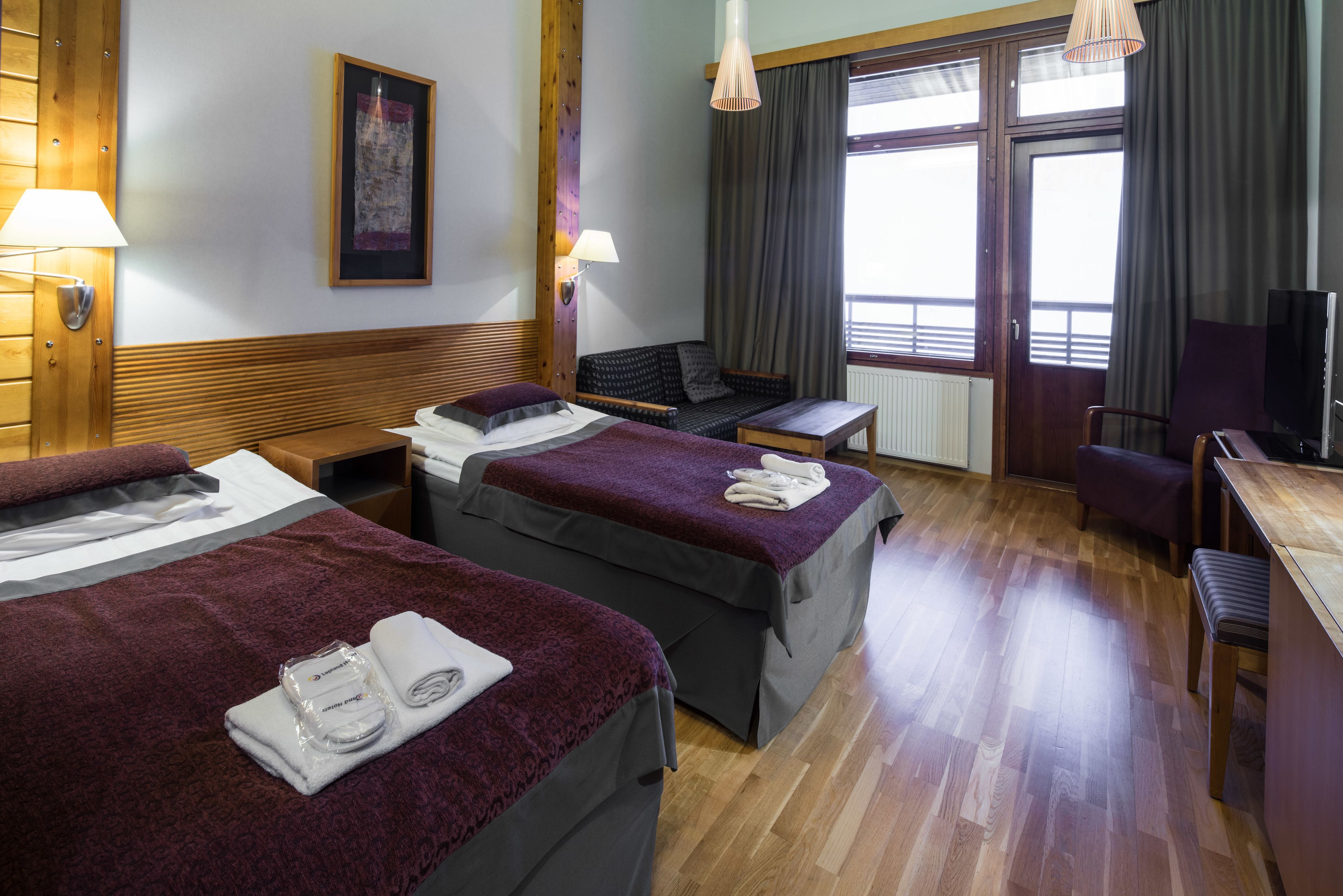 A hotel room with two beds, a desk, a chair, a TV, and a window with curtains.