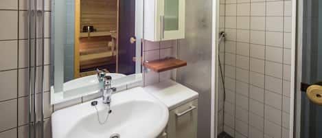 Un baño con lavamanos blanco, un espejo, estante de madera y zona de ducha.