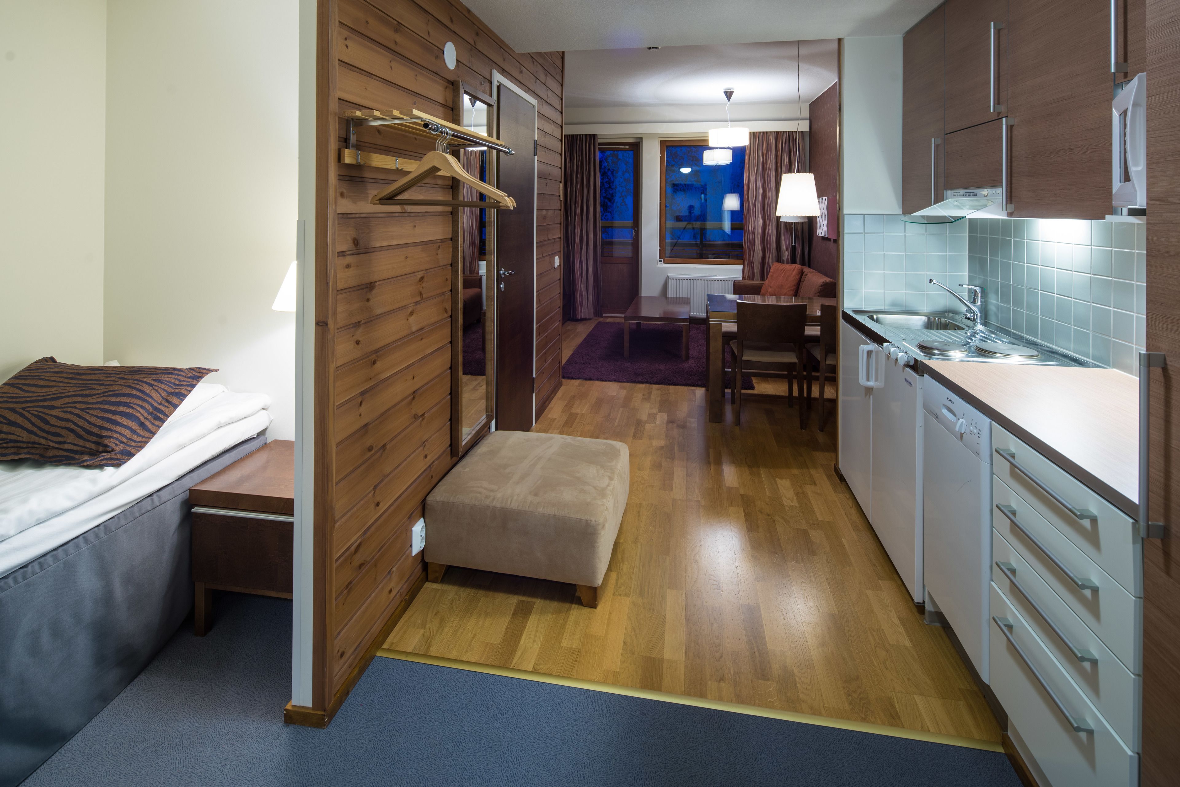 A compact hotel room with a bed, a small seating area, a kitchenette, and a bathroom.