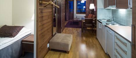 A compact hotel room with a bed, a small seating area, a kitchenette, and a bathroom.