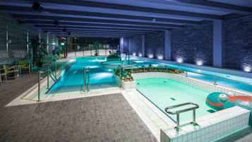 Swim laps in a spacious pool with multiple lanes and a central water slide, surrounded by a deck area with safety railings.