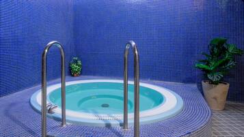Un jacuzzi con escalones metálicos y un interior azulado de azulejos, rodeado por un techo y paredes de madera.