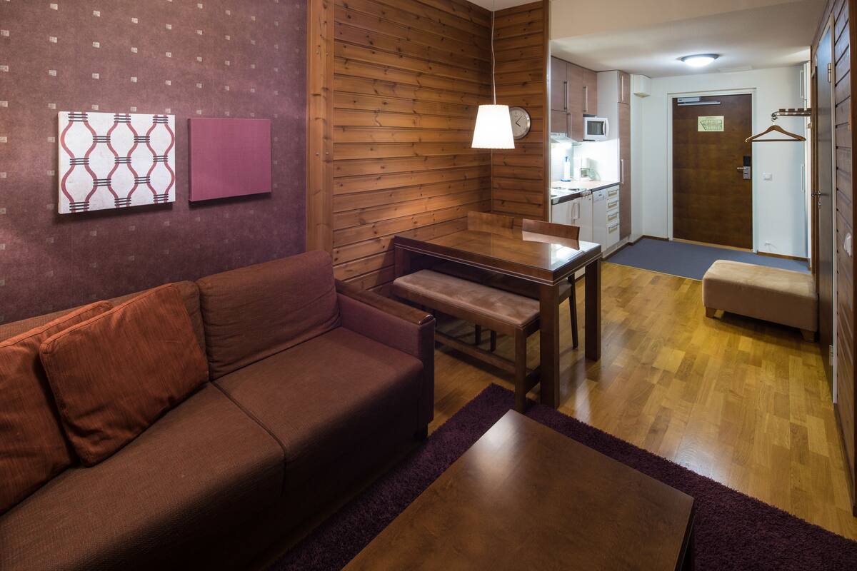 A modern living room with a brown sofa, a wooden dining table, and a hanging lamp.