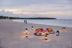 A beach setting with a sofa and lanterns, a couple walking, and a calm sea.