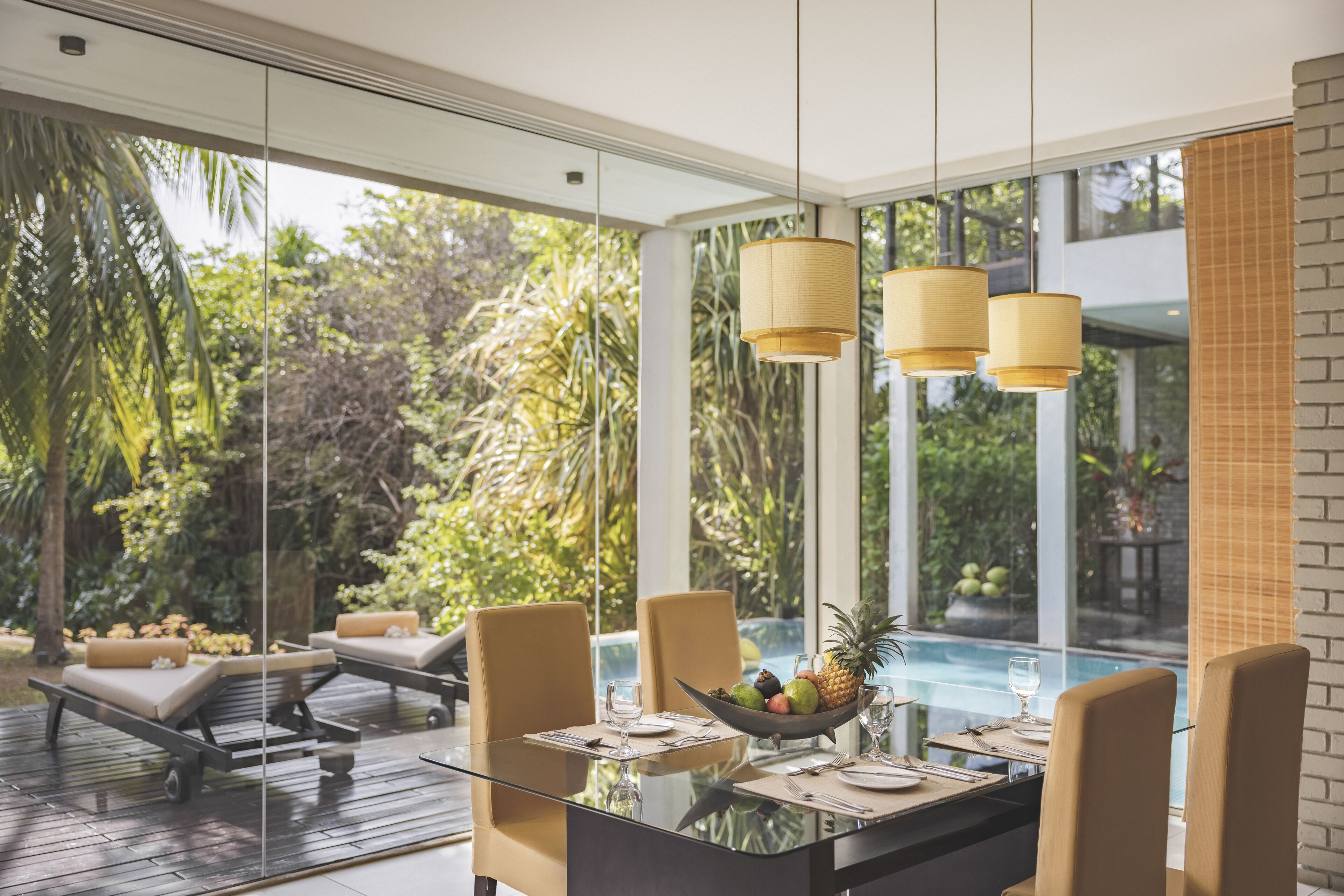 A modern dining area with a glass table, chairs, and a fruit bowl.