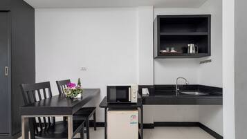 Cocina compacta con una mesa de comedor, sillas, microondas, refrigerador pequeño, pileta y estante con utensilios de cocina.