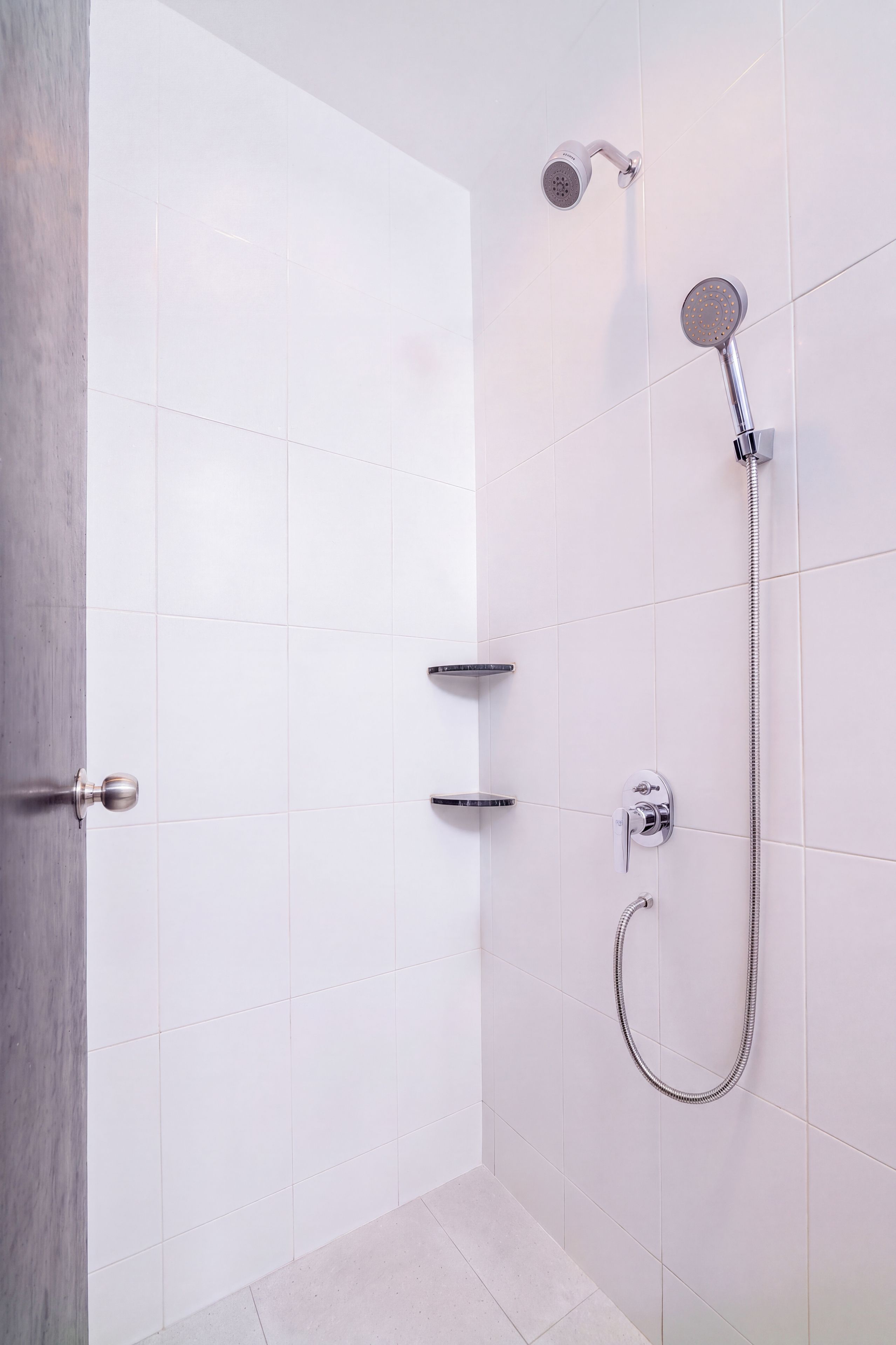 Een moderne badkamer met witte tegels, een douche met een handdouche en een muurbevestigde kraan.