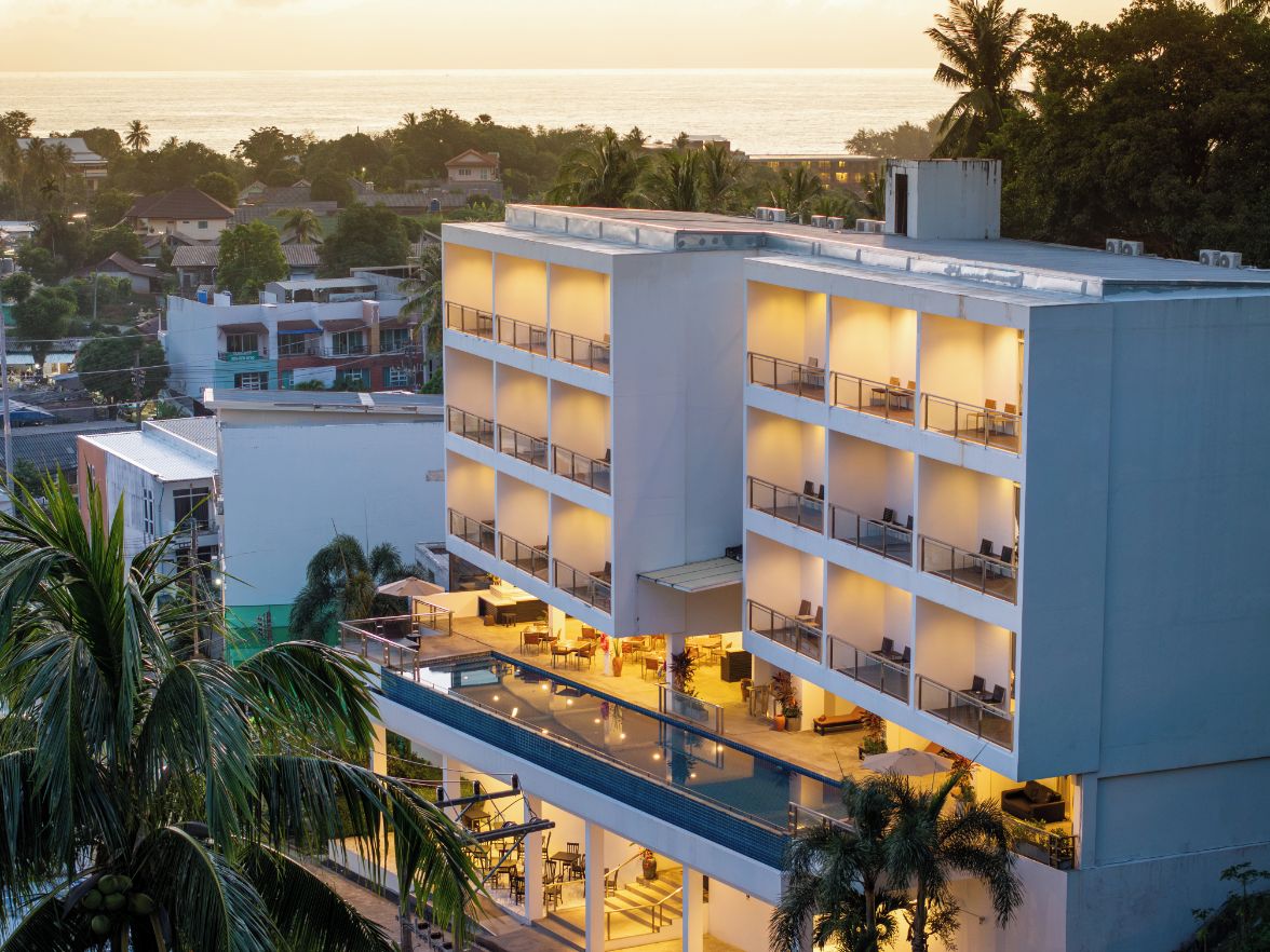 A multi-story hotel with balconies, a pool, and a view of the ocean.