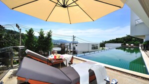 A rooftop pool area with lounge chairs, a table with drinks, and a large umbrella providing shade. - Laelay Suites (Karon)