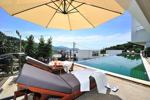 Ein Poolbereich auf dem Dach mit Liegestühlen, einem Tisch mit Getränken und einem großen Sonnenschirm, der Schatten spendet.