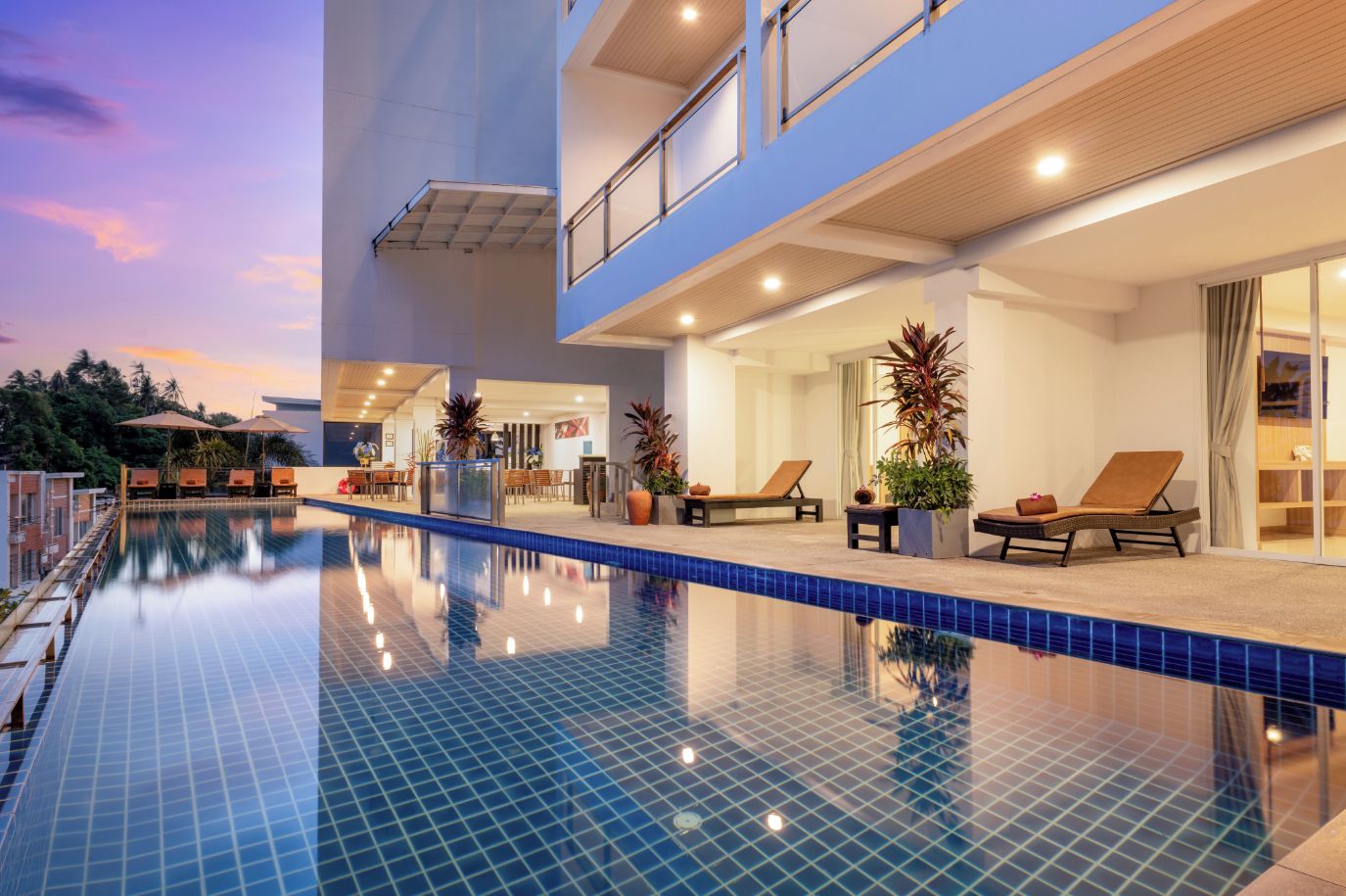 Un hotel moderno con piscina, sillones de descanso y zona de restaurante.