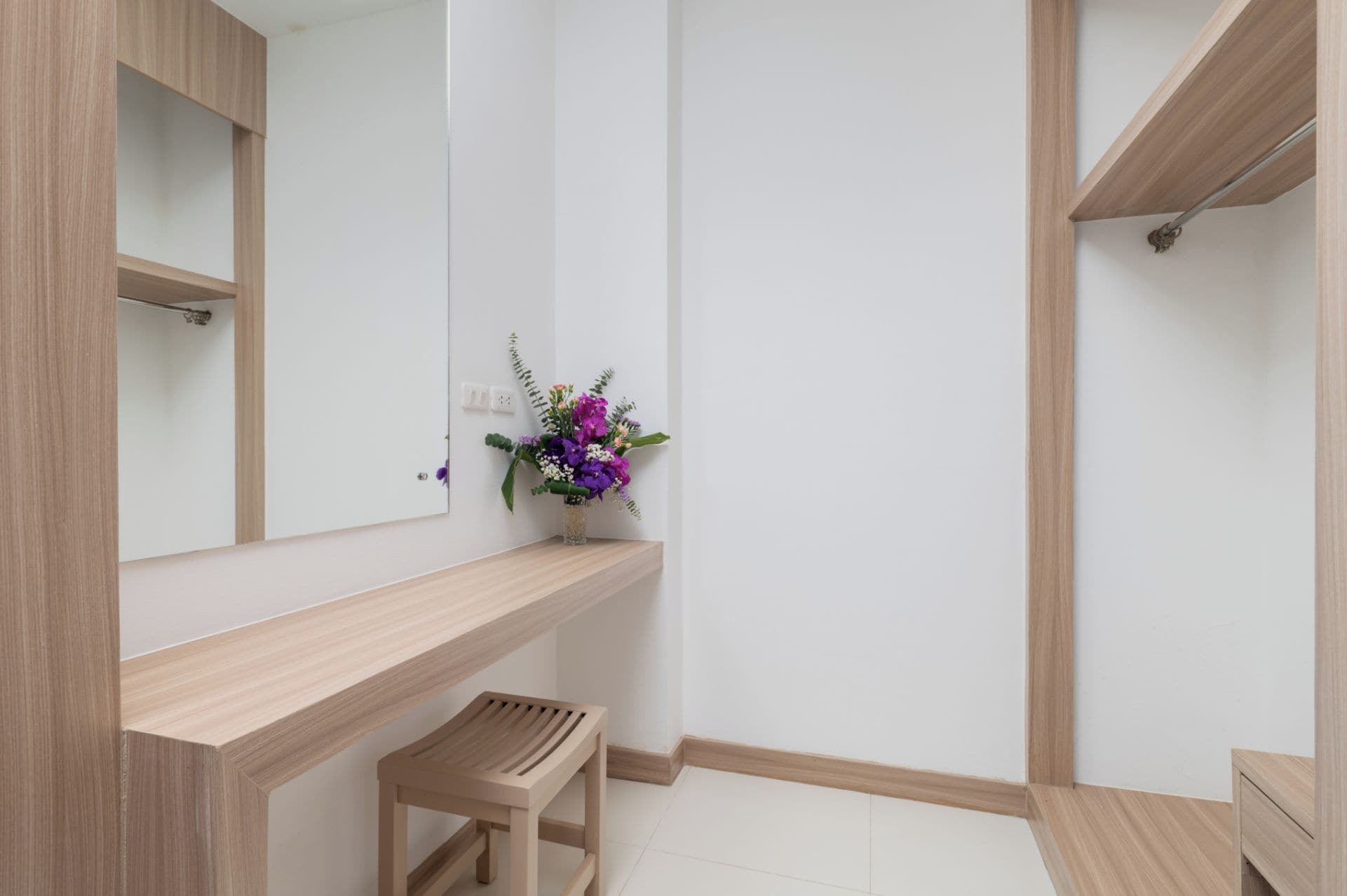 Ein modernes Badezimmer mit einem Holzwaschtisch, einem Spiegel, einem kleinen Hocker und einem an der Wand befestigten Regal.
