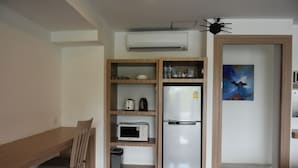 A compact kitchen with a microwave, refrigerator, and wooden shelves. - Laelay Suites (Karon)