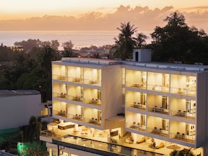 Hotel de diverses plantes amb balcons, una zona de piscina i vistes al mar al capvespre.