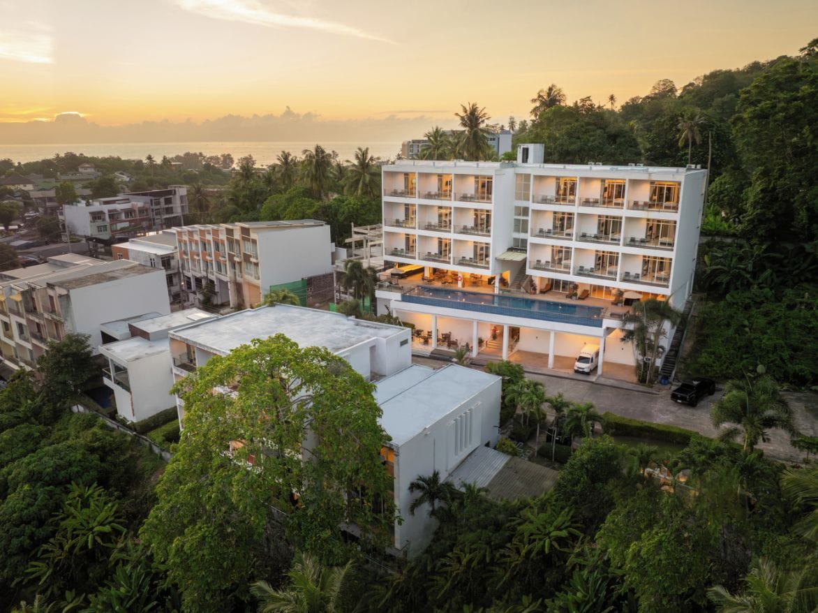 A multi-story hotel with balconies, a swimming pool, and a view of the sea.