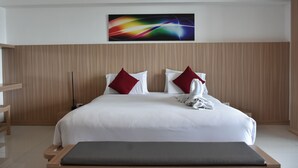 A modern hotel room with a large bed, wooden headboard, and a colorful abstract painting above the bed. - Laelay Suites (Karon)