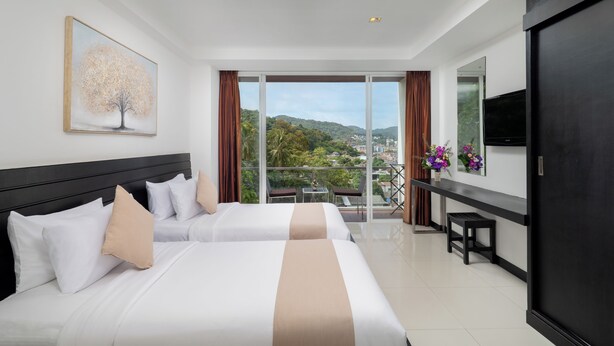 Habitación de hotel con dos camas, un ventanal con vistas a la ciudad, un televisor de pantalla plana y un escritorio con una silla.