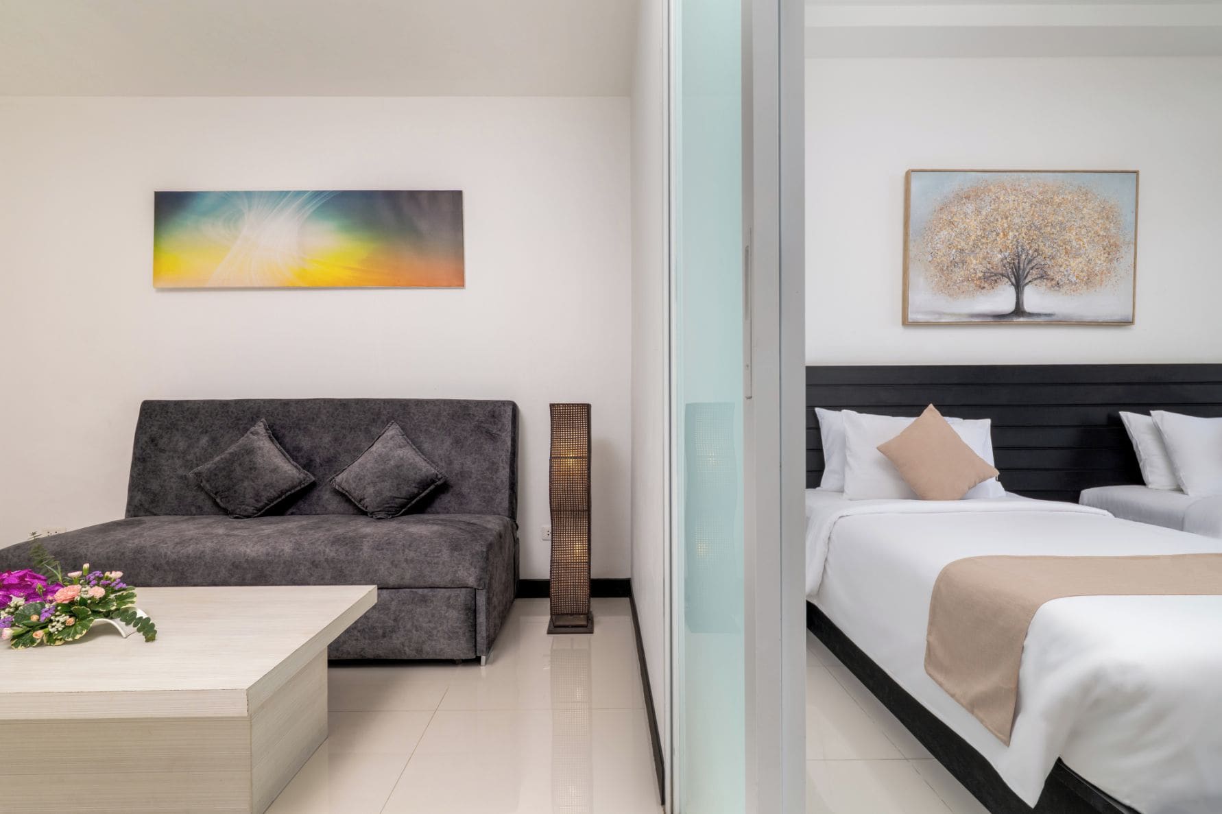 Habitación de hotel con sofá, cama, mesita de noche con flores y dos obras de arte colgadas en la pared.