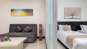 Habitación de hotel con sofá, cama, mesita de noche con flores y dos obras de arte colgadas en la pared.