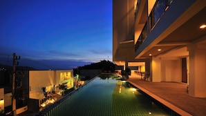 A modern building with a swimming pool, a covered walkway, and a view of the surrounding area. - Laelay Suites (Karon)