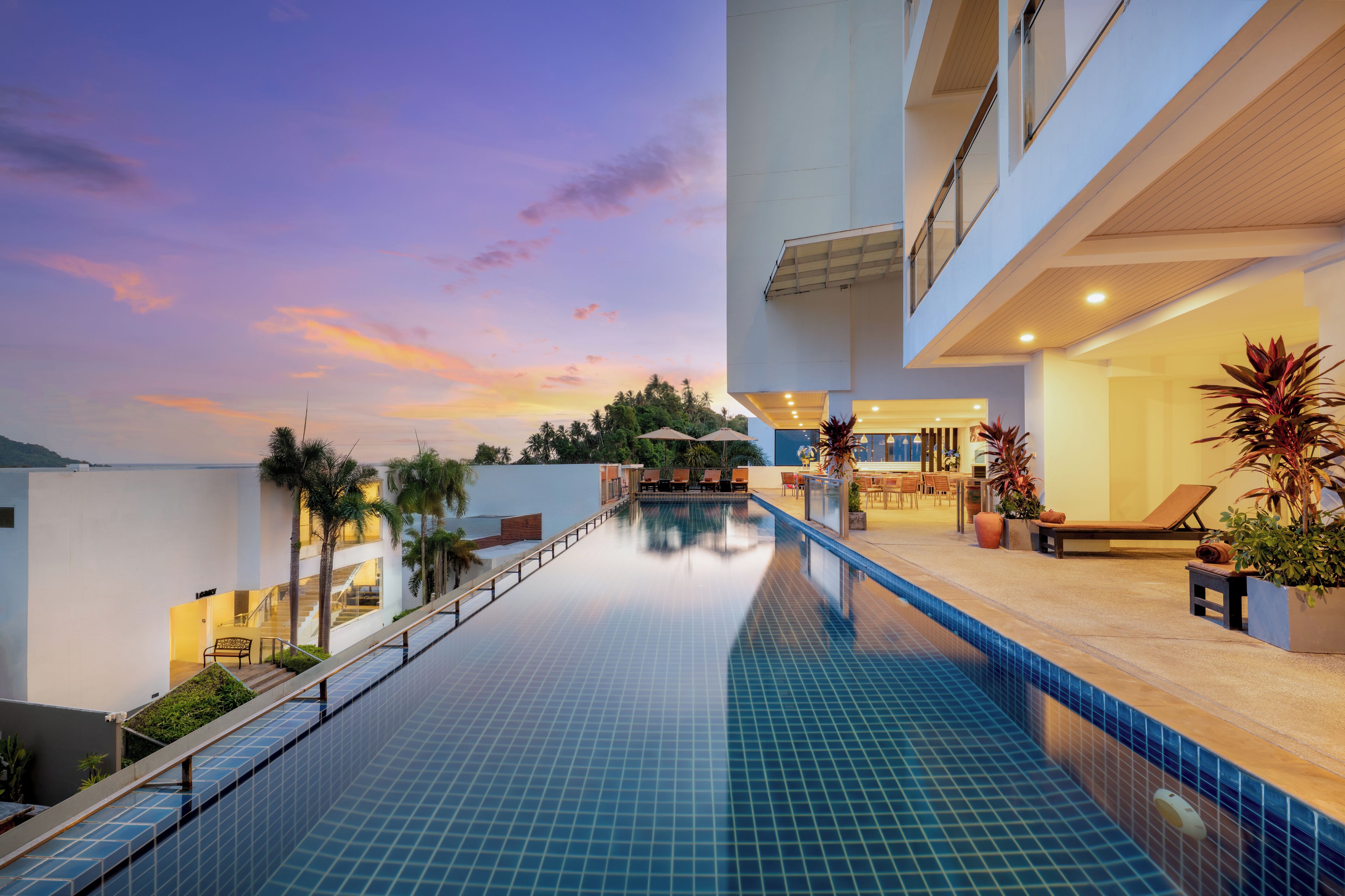 A modern hotel with a pool, lounge area, and a view of the sunset.