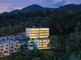 A multi-story hotel with balconies, surrounded by lush greenery and hills.
