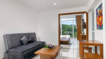 Una habitación de hotel moderna con un sofá gris, una mesa de centro de madera, una cama con vistas y un cuadro en la pared.