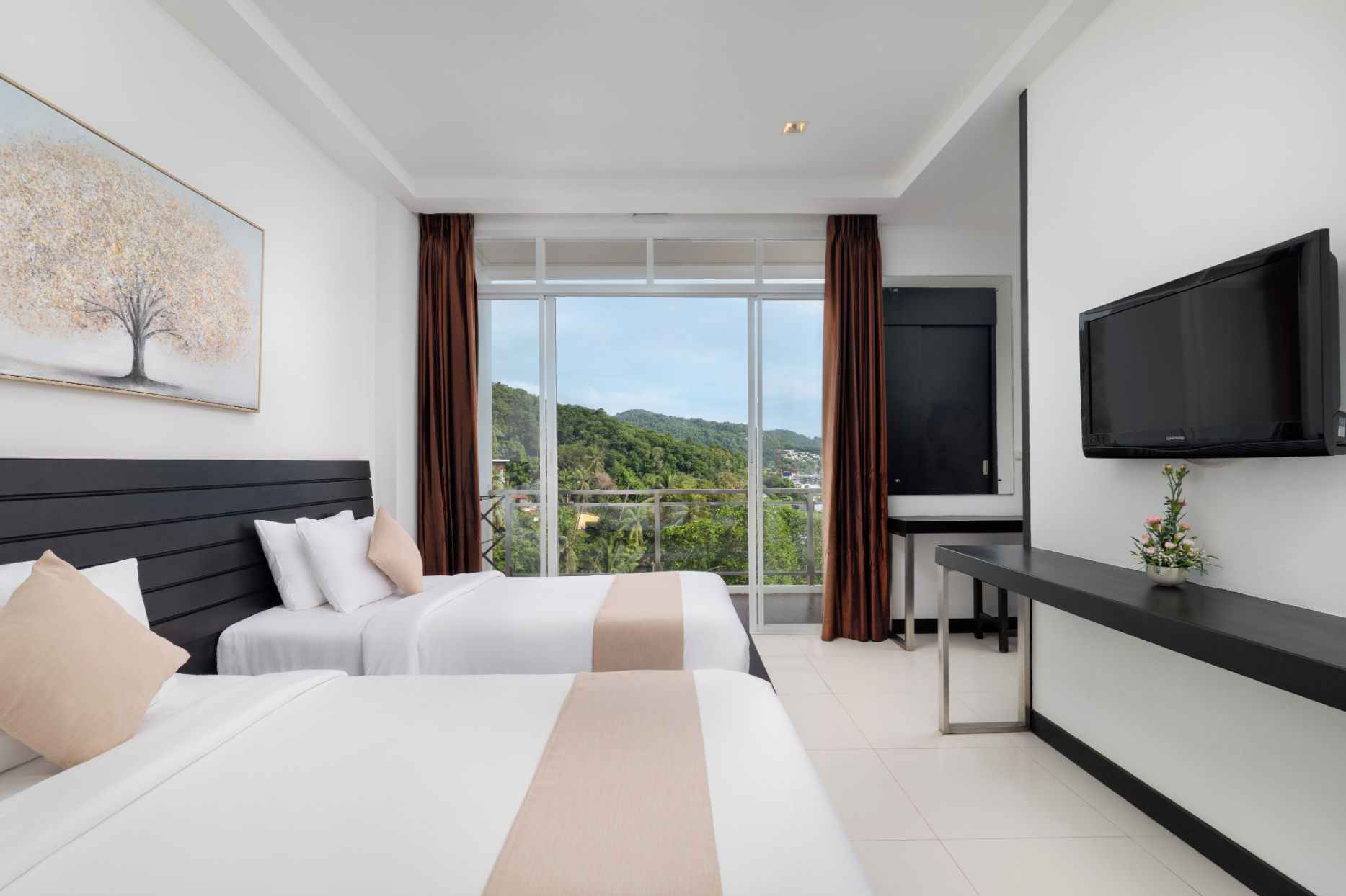 Habitación de hotel con dos camas, televisión y balcón con vistas a las colinas.