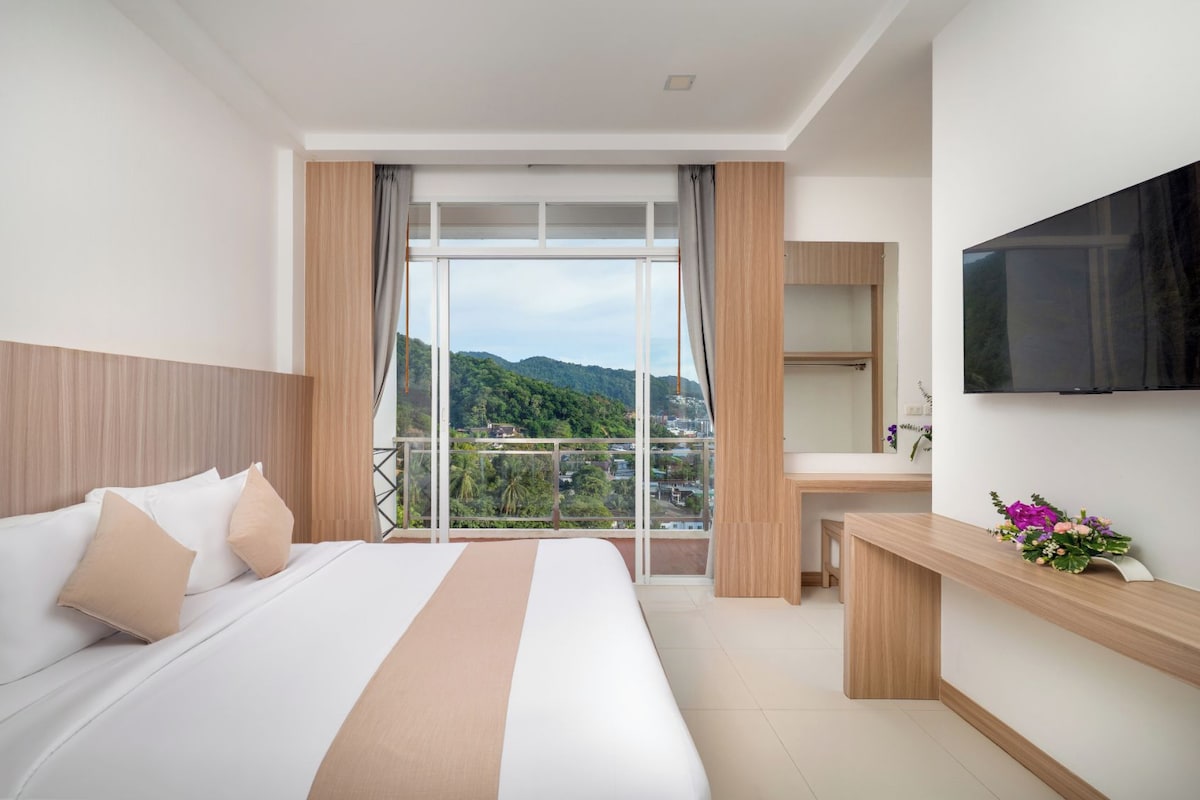 Ein Hotelzimmer mit einem großen Bett, einem Schreibtisch, einem Fernseher und einem Balkon mit Bergblick.