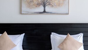 Una habitación de hotel con dos camas, un cabecero oscuro y un cuadro de un árbol en la pared.