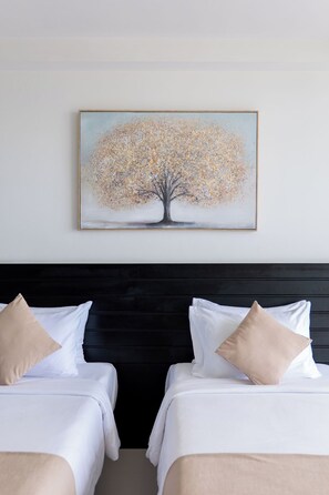 Una habitación de hotel con dos camas, un cabecero oscuro y un cuadro de un árbol en la pared.