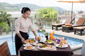 Habitación de hotel con piscina, mesa dispuesta para el desayuno y vista a la ciudad.