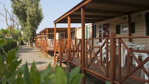 A row of wooden cabins with outdoor seating areas, surrounded by trees. - New Camping Le Tamerici (Cecina)