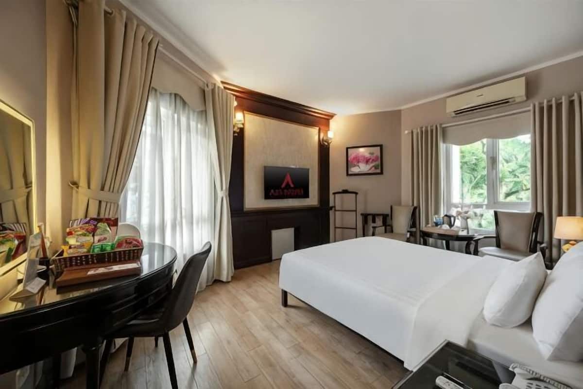 A hotel room with a bed, desk, chair, TV, and window with curtains.