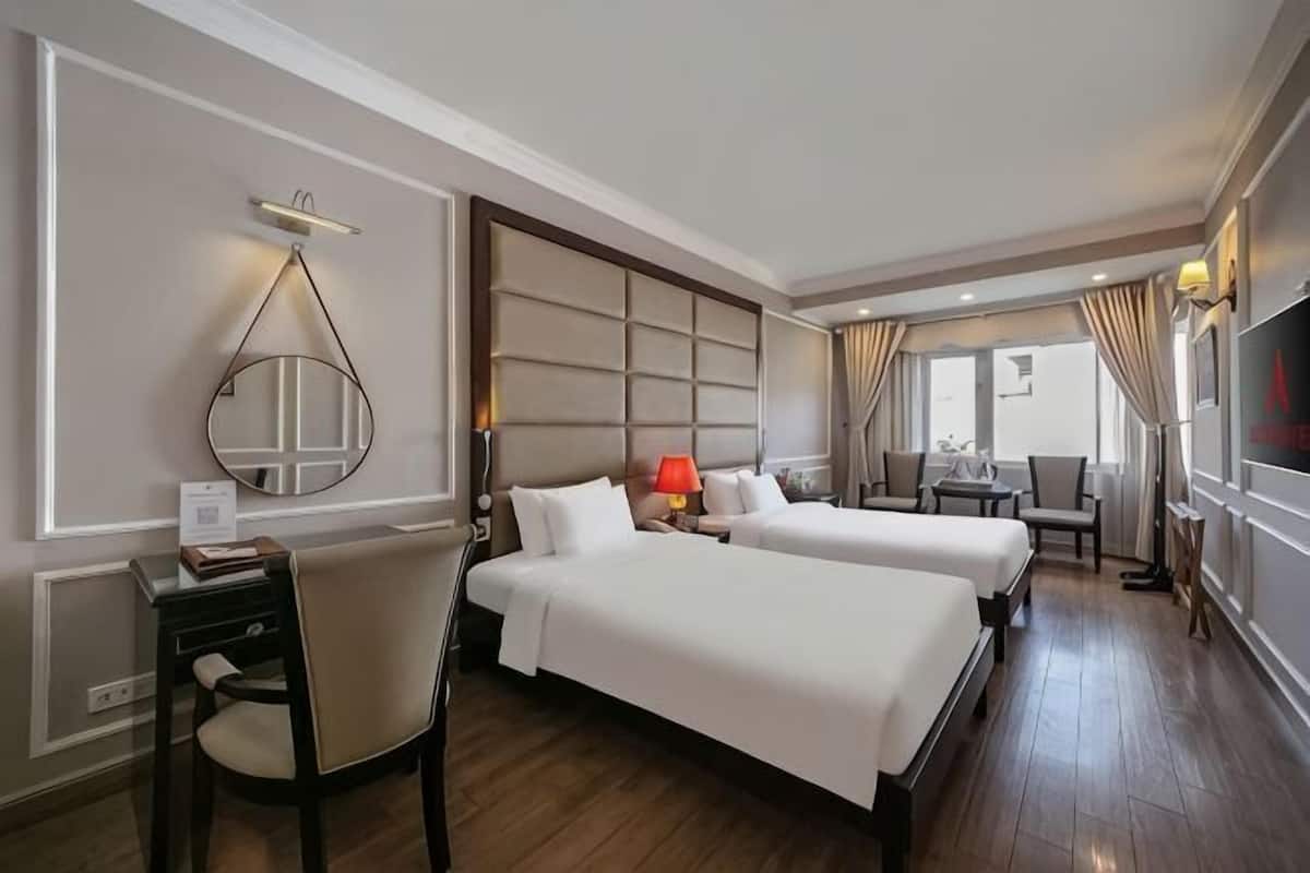 A hotel room with two beds, a desk, a chair, a TV, and a window.