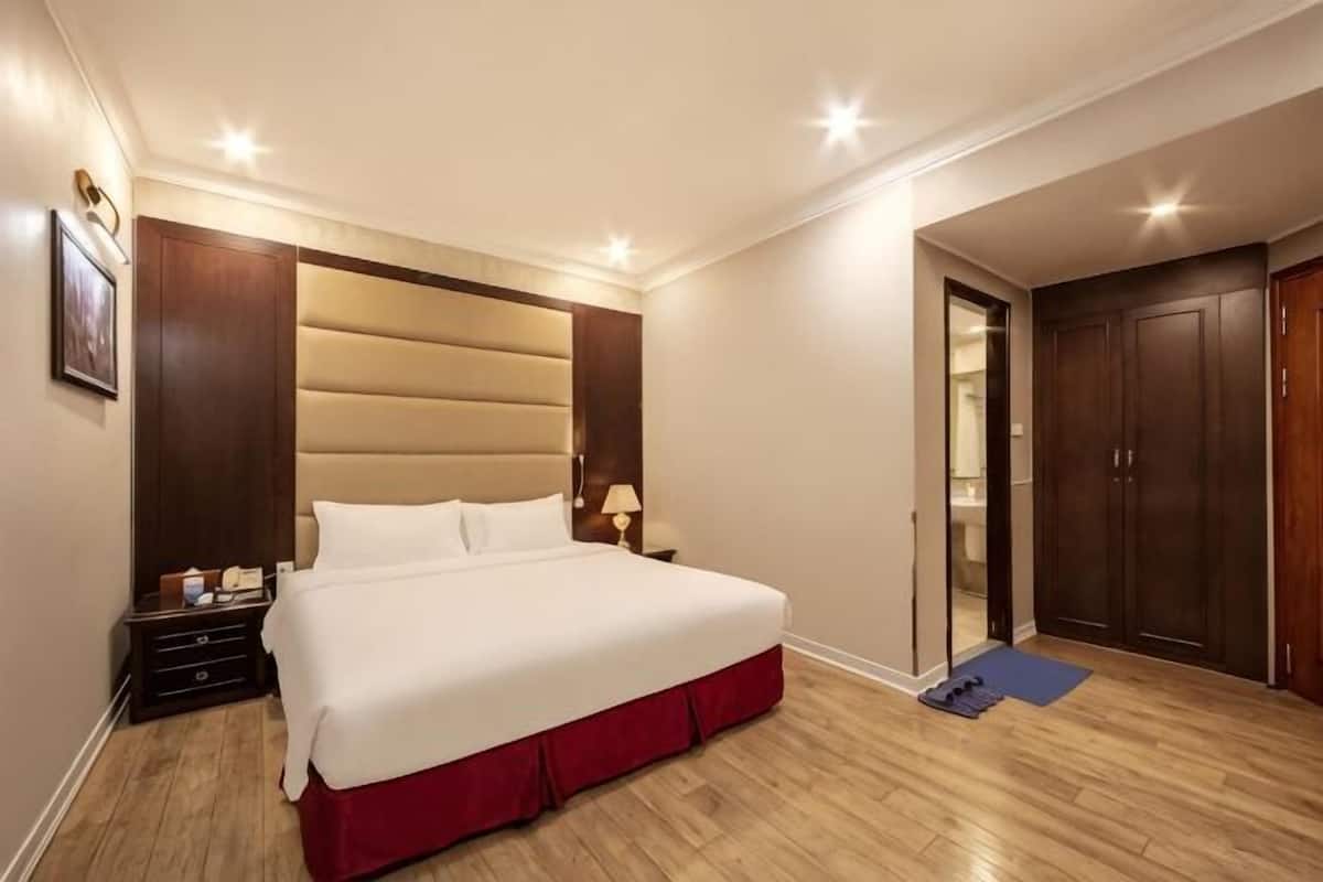 A hotel room with a large bed, wooden flooring, a wardrobe, and a door leading to a bathroom.