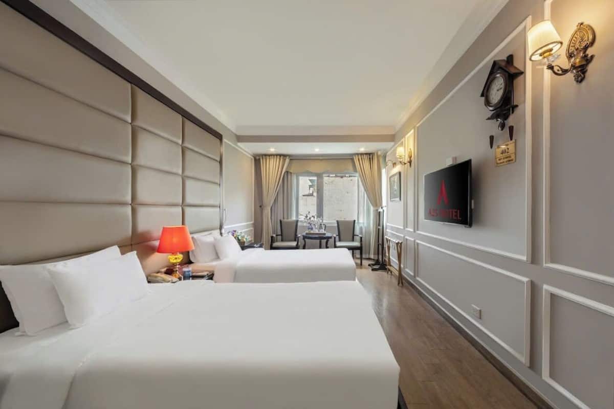 A hotel room with two beds, a television, a desk with a chair, and a view of the outside.