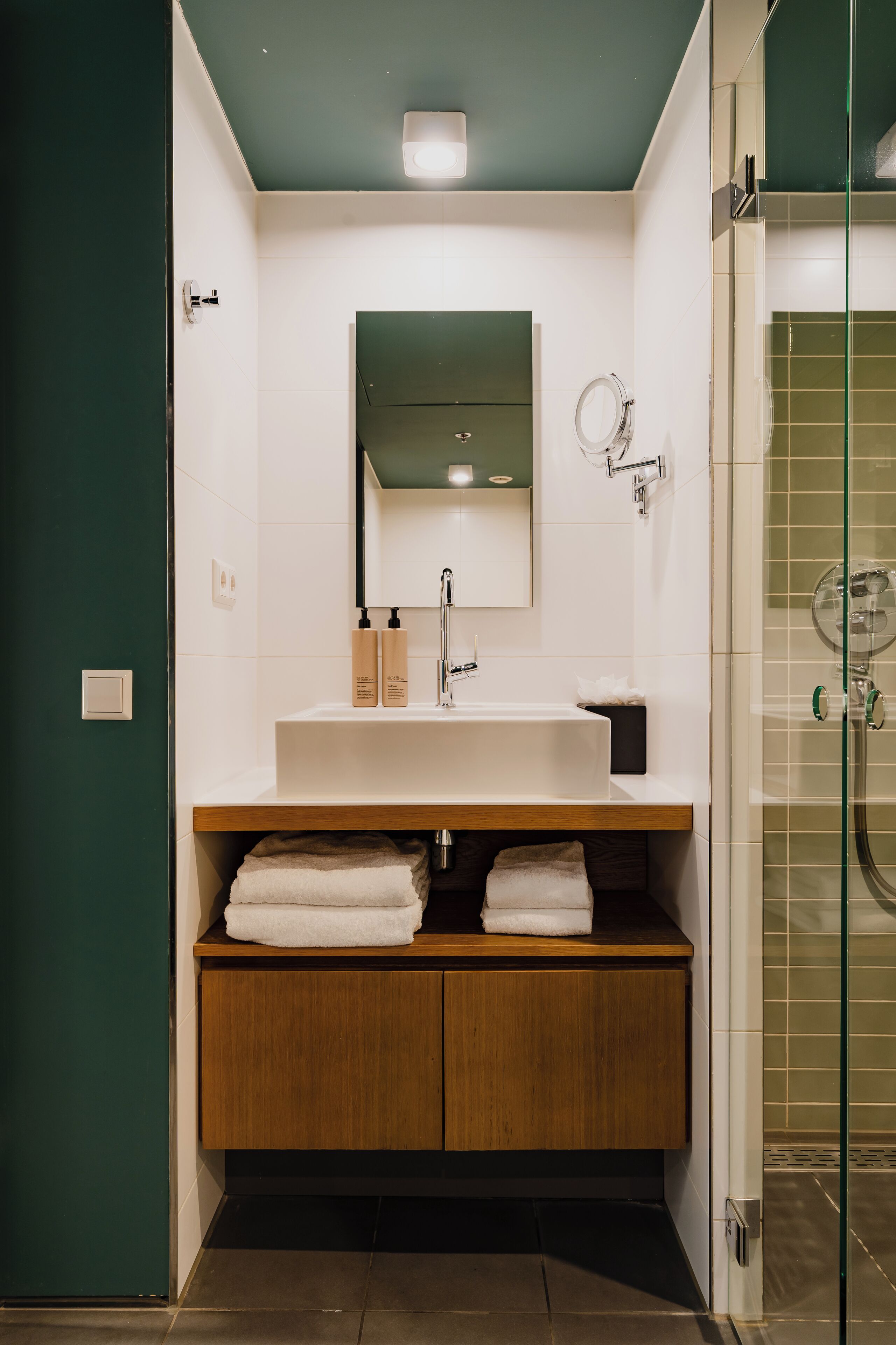 Un baño moderno con tocador de madera, lavamanos blanco y cabina de ducha de vidrio.