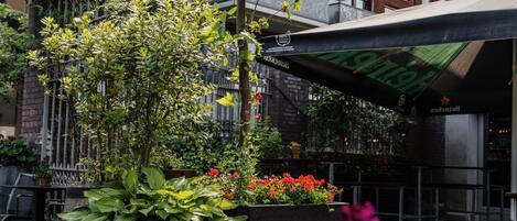 Un espacio al aire libre con mesas y plantas en macetas, rodeado de edificios con balcones y fachada de ladrillo.
