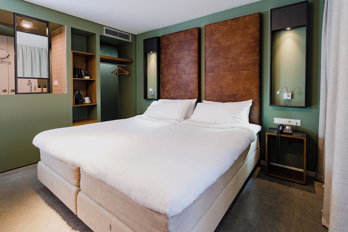 A large bed with white linens, a wooden headboard, a bedside table with a phone, and a mirror above the bed.