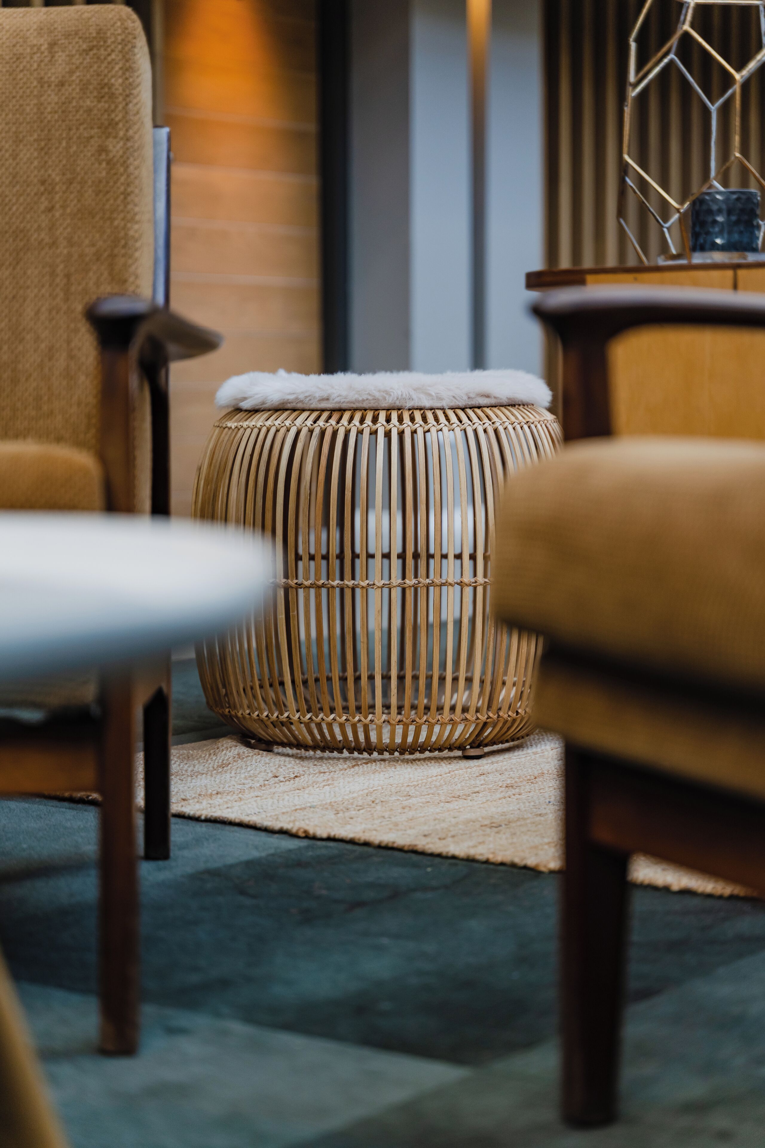 Ein Hocker aus Weidengeflecht mit weißem Kissen, ein Holzstuhl und ein kleiner Tisch mit einem blauen Gegenstand darauf.