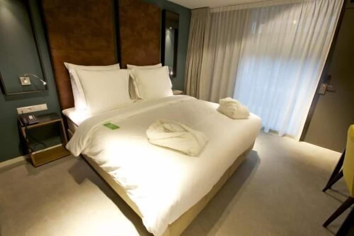 A hotel room with a bed, a nightstand, a lamp, and a window with curtains.