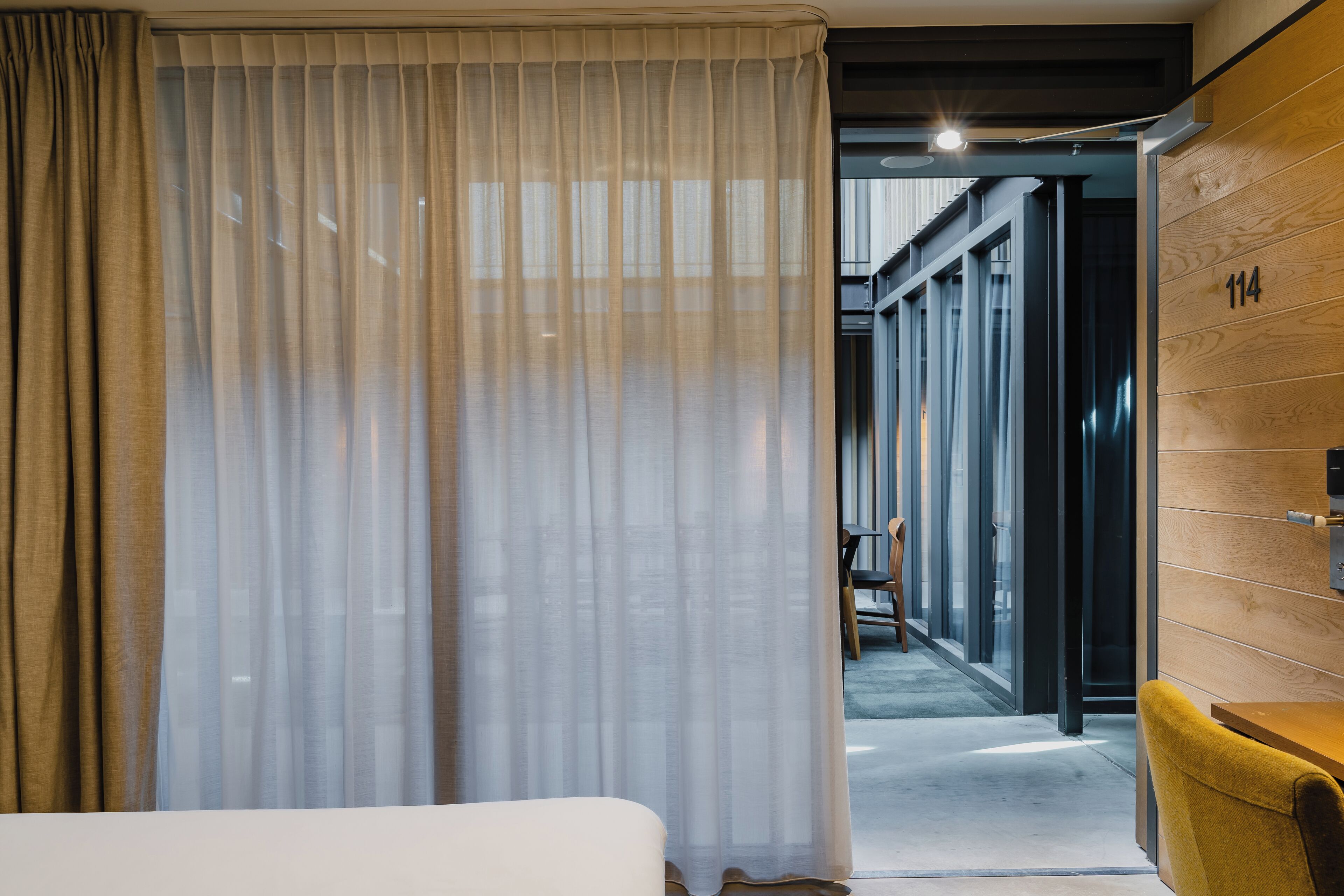 Habitación de hotel con una cama, una silla amarilla y una pared de madera con un número.