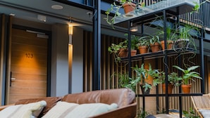 A modern hotel room with a leather sofa, a glass-enclosed balcony with potted plants, and a wooden door labeled "103".