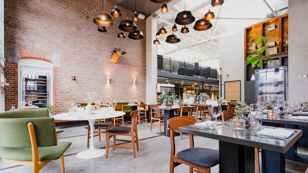A spacious dining area with brick walls, hanging pendant lights, and a variety of seating options.