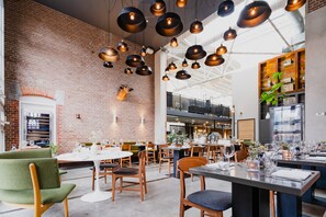 A spacious dining area with brick walls, hanging pendant lights, and a variety of seating options. - Hotel De Hallen (Amsterdam)