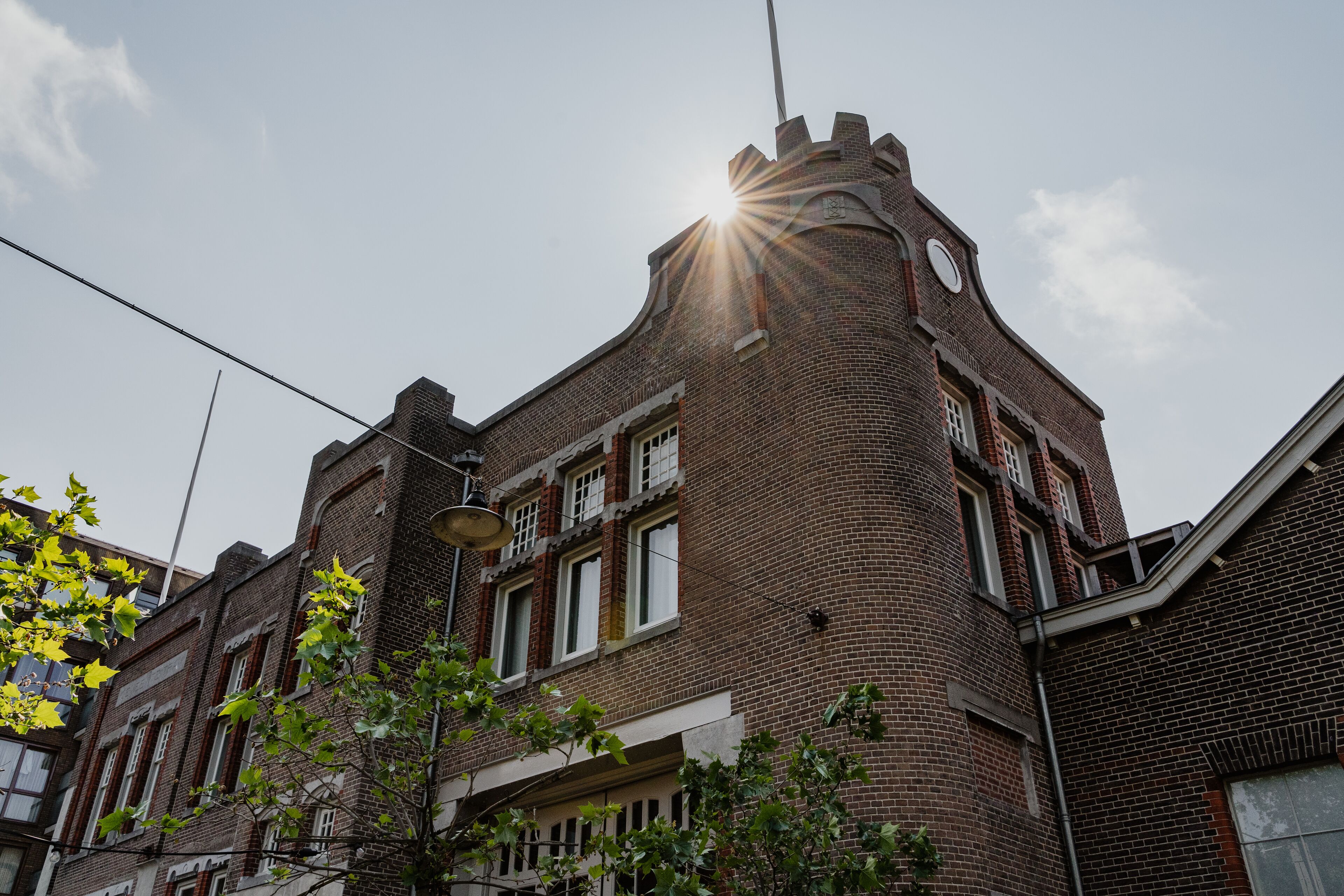 Un bâtiment en briques doté d’une tourelle et d’un clocher, avec de nombreuses fenêtres et un lampadaire visible dans la rue.