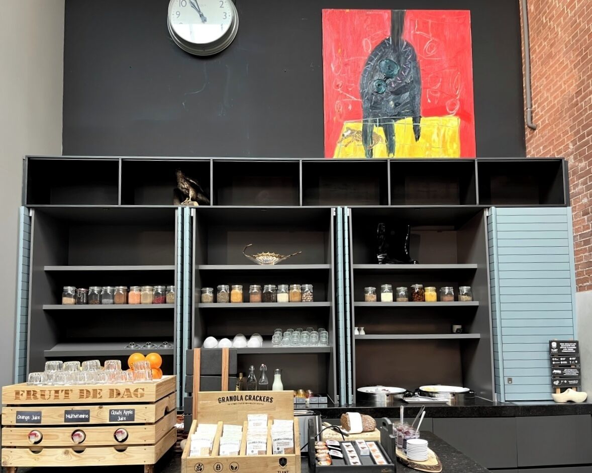 A café with shelves stocked with jars of condiments, a clock, and a painting on the wall.